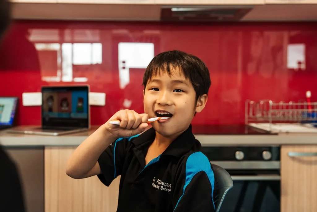 A young boy smiling while brushing his teeth wearing a school uniform